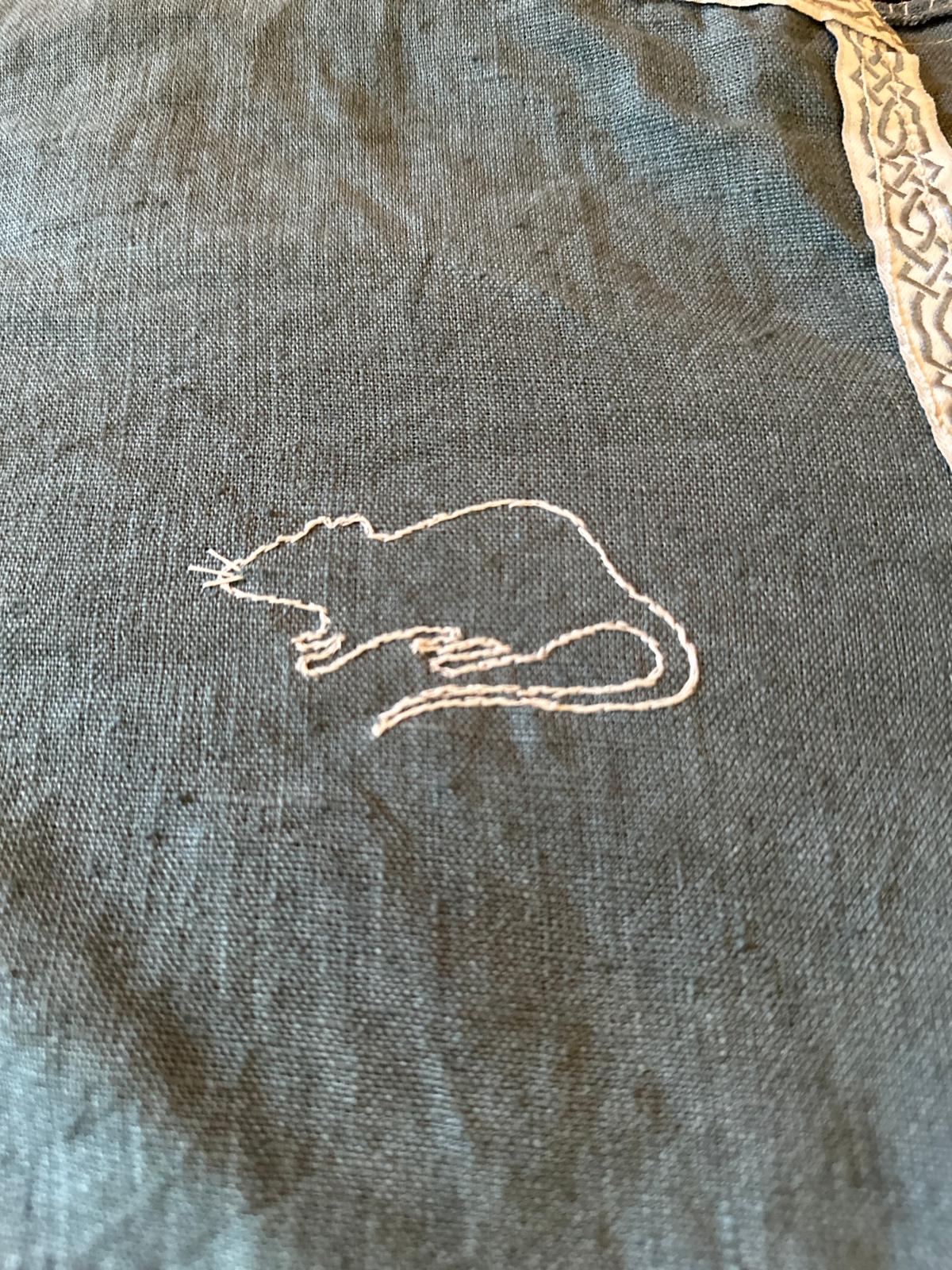 A rat embroidered on light blue linen with white thread